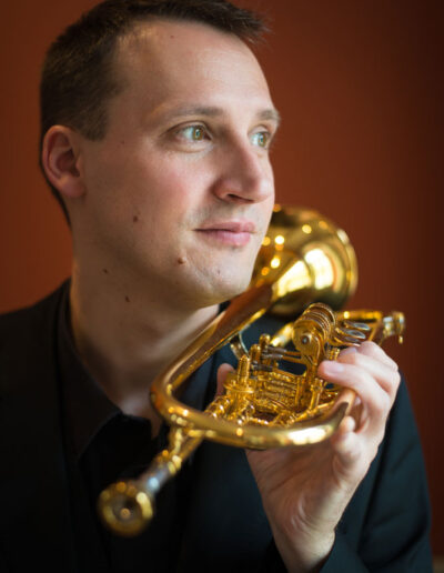 Portrait in dem Joachim eine Trompete unter sein Kinn hält und lächelnd zur Seite guckt.